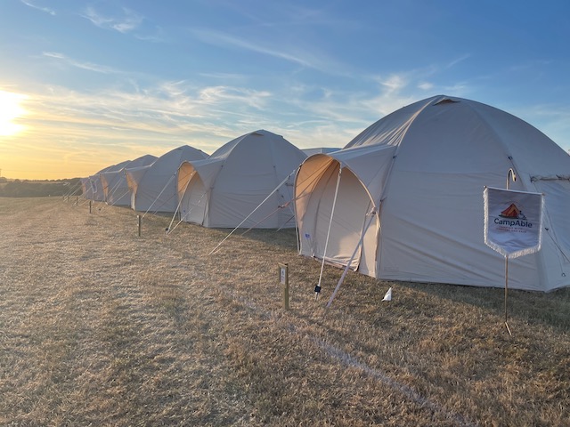 A CampAble accessible tent pitched at a festival, flying a CampAble flag